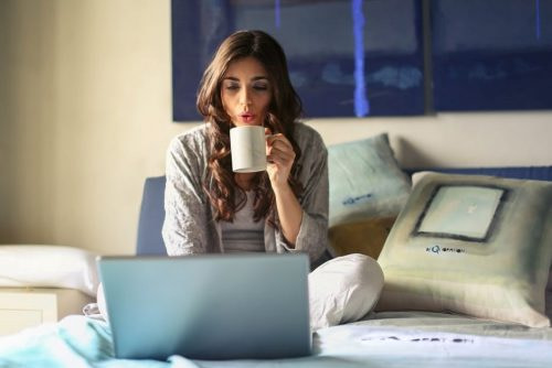 woman sipping coffee on bed with laptop